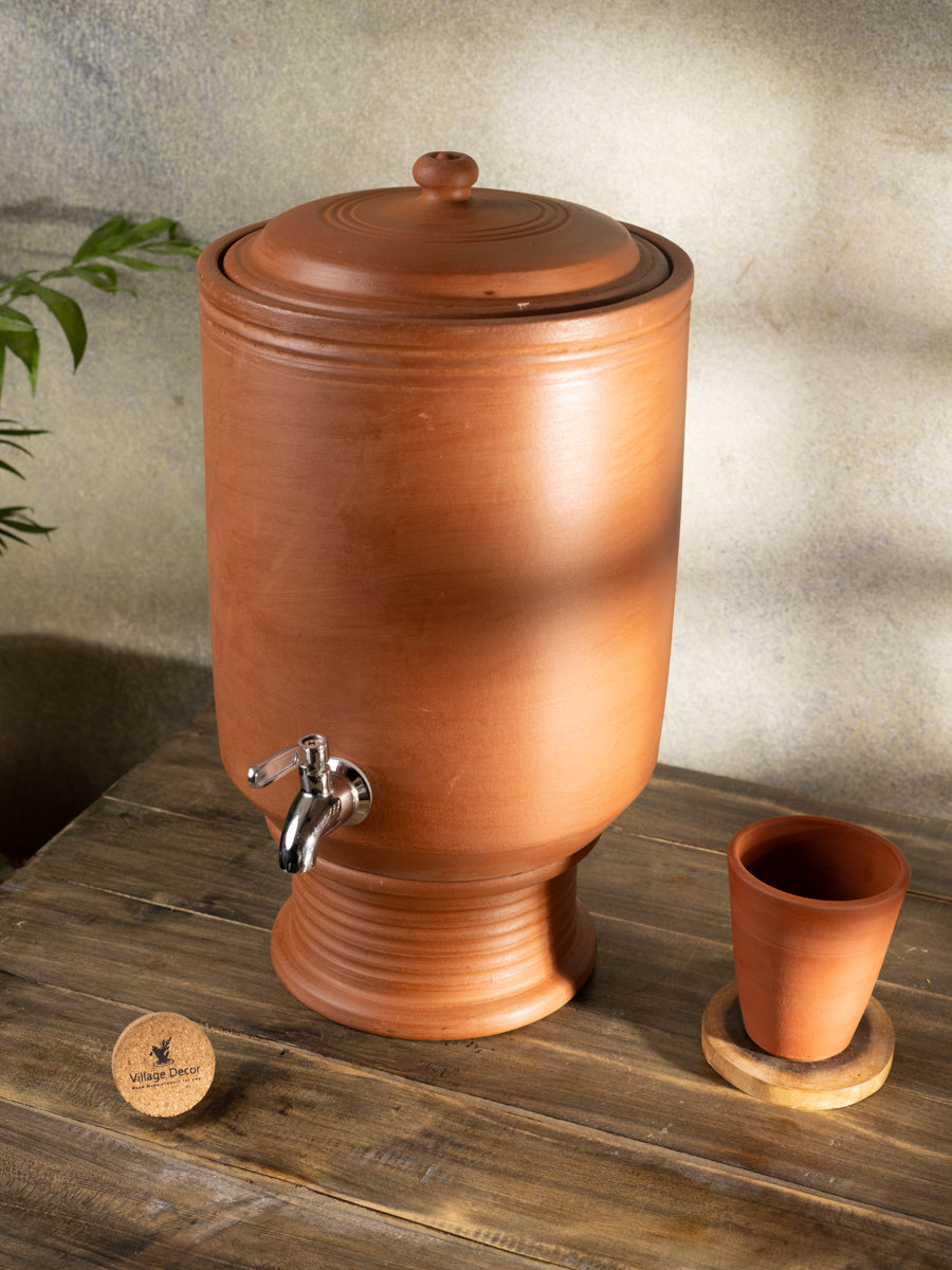 Terracotta water dispenser with a small glass on a wooden surface