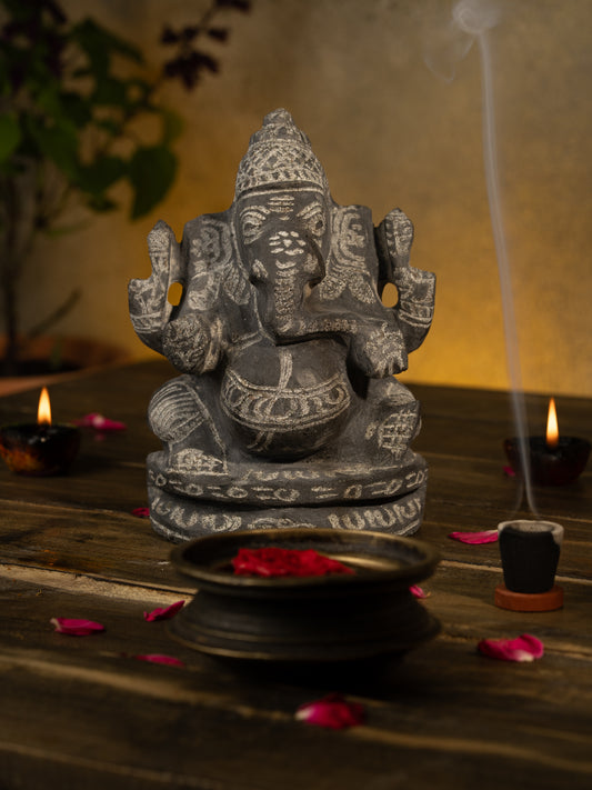 Black Stone Vinayagar Idol in Traditional Pooja Setup with Diyas, Rose Petals, and Tulsi Plant for Home Decor or Vastu Placement.