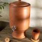 Terracotta water dispenser with a small glass  on a wooden surface