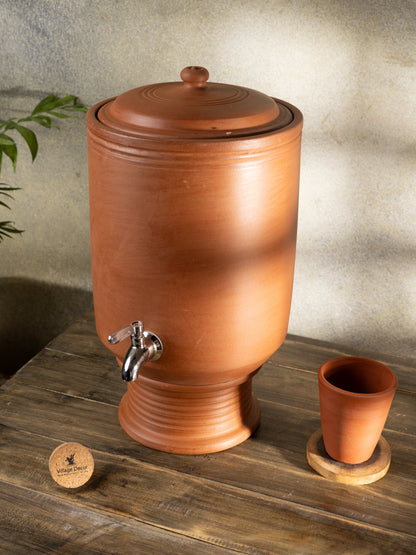 Terracotta water dispenser with a small glass  on a wooden surface